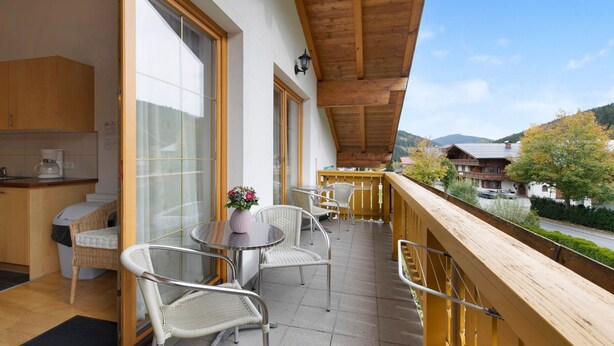 A balcony with a wooden railing, a table with chairs, and a view of a mountain landscape.
