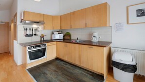 A compact kitchen with wooden cabinets, a microwave, a stove, and a trash bin.