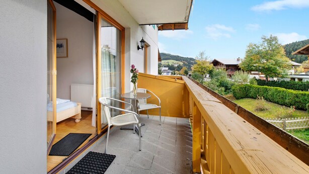 A balcony with a wooden railing, a small table with chairs, a bed with a window, and a view of a green landscape. - "Haus Lowe Appartement 1 Stock Nr 2" with Mountain View (Filzmoos)
