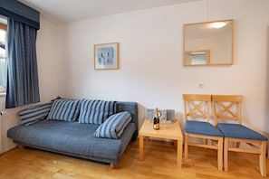 Ein Zimmer mit einer Couch, einem Holzstuhl, einem kleinen Tisch mit Flasche und Gläsern, einem gerahmten Bild und einem Spiegel.