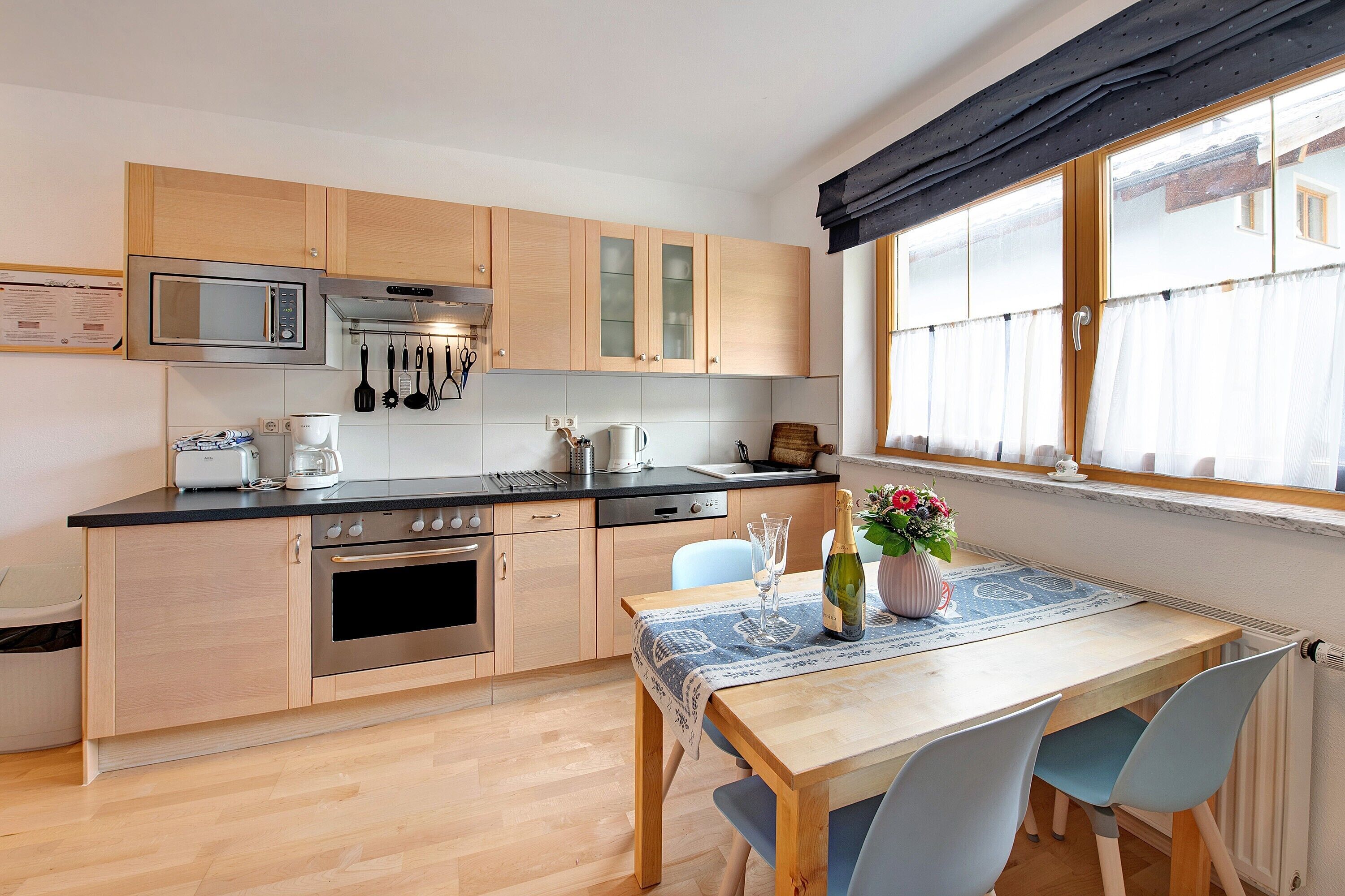 A modern kitchen with wooden cabinets, a stainless steel microwave, and a dining area with a table and chairs.