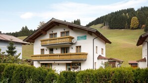 Un edificio de dos pisos con balcones, un letrero que indica un restaurante y un paisaje montañoso al fondo.