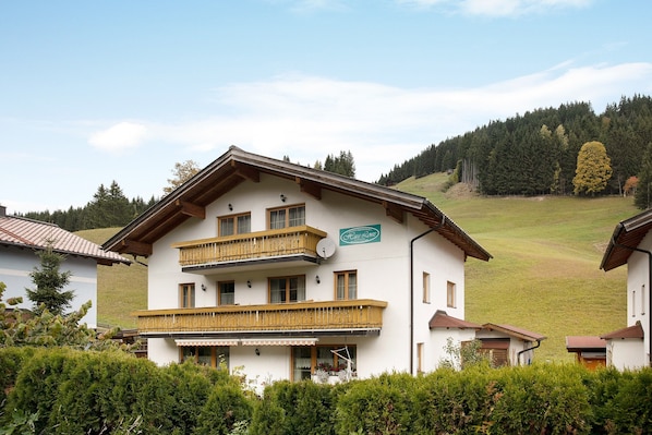 A two-story building with balconies, a sign indicating a restaurant, and a hilly landscape in the background.