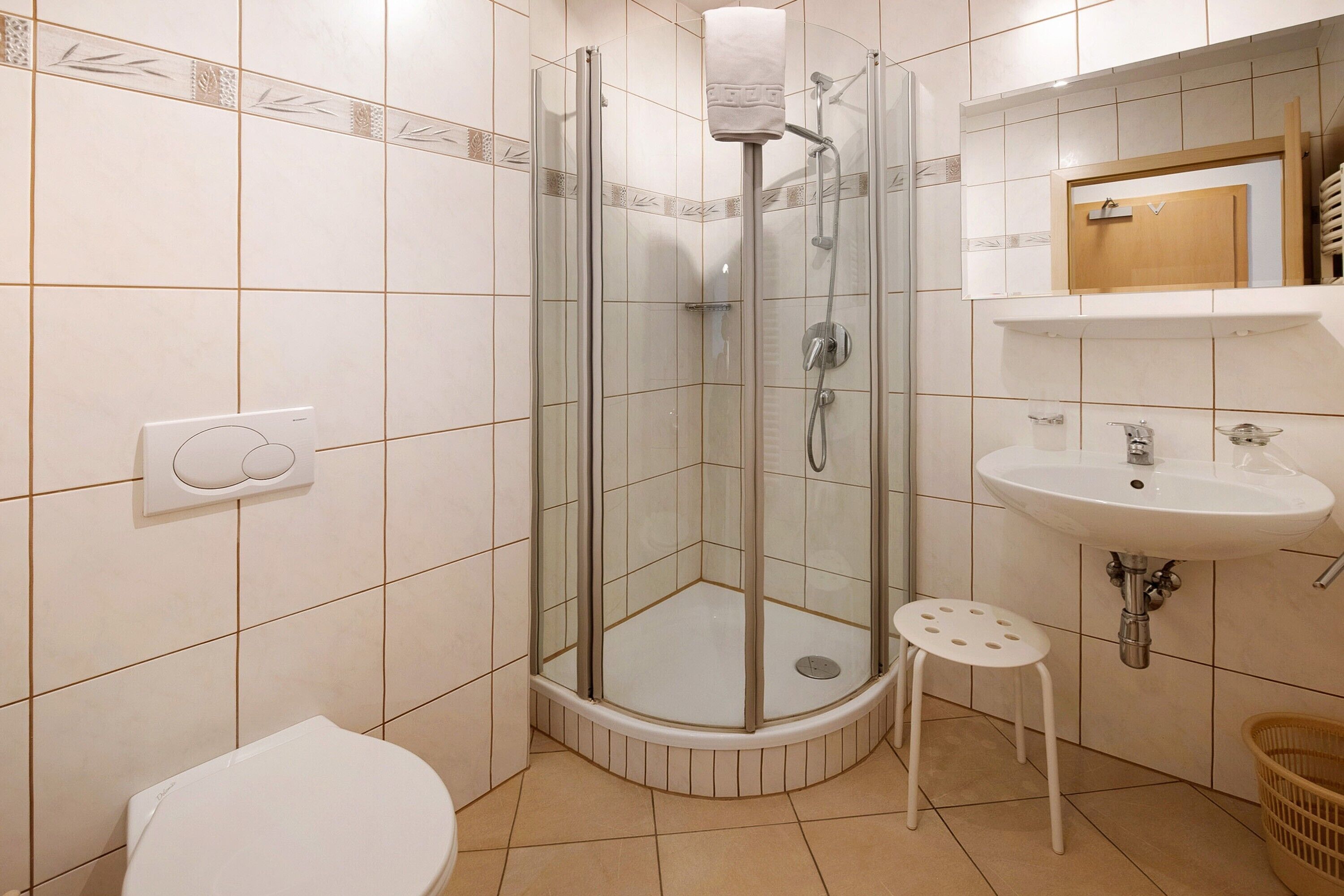 Een badkamer met een douche met glazen wand, een toilet, een wastafel en een klein krukje.