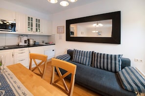 A modern kitchen with white cabinets, a dining table with chairs, and a dark blue sofa with striped cushions.