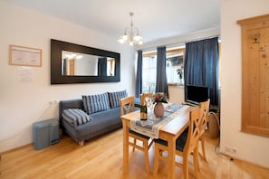 A room with a sofa, a dining table with chairs, a mirror, a chandelier, a television, and a cabinet.