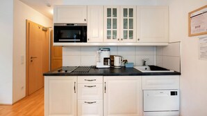Una cocina compacta con gabinetes blancos, microondas, cafetera y lavavajillas.
