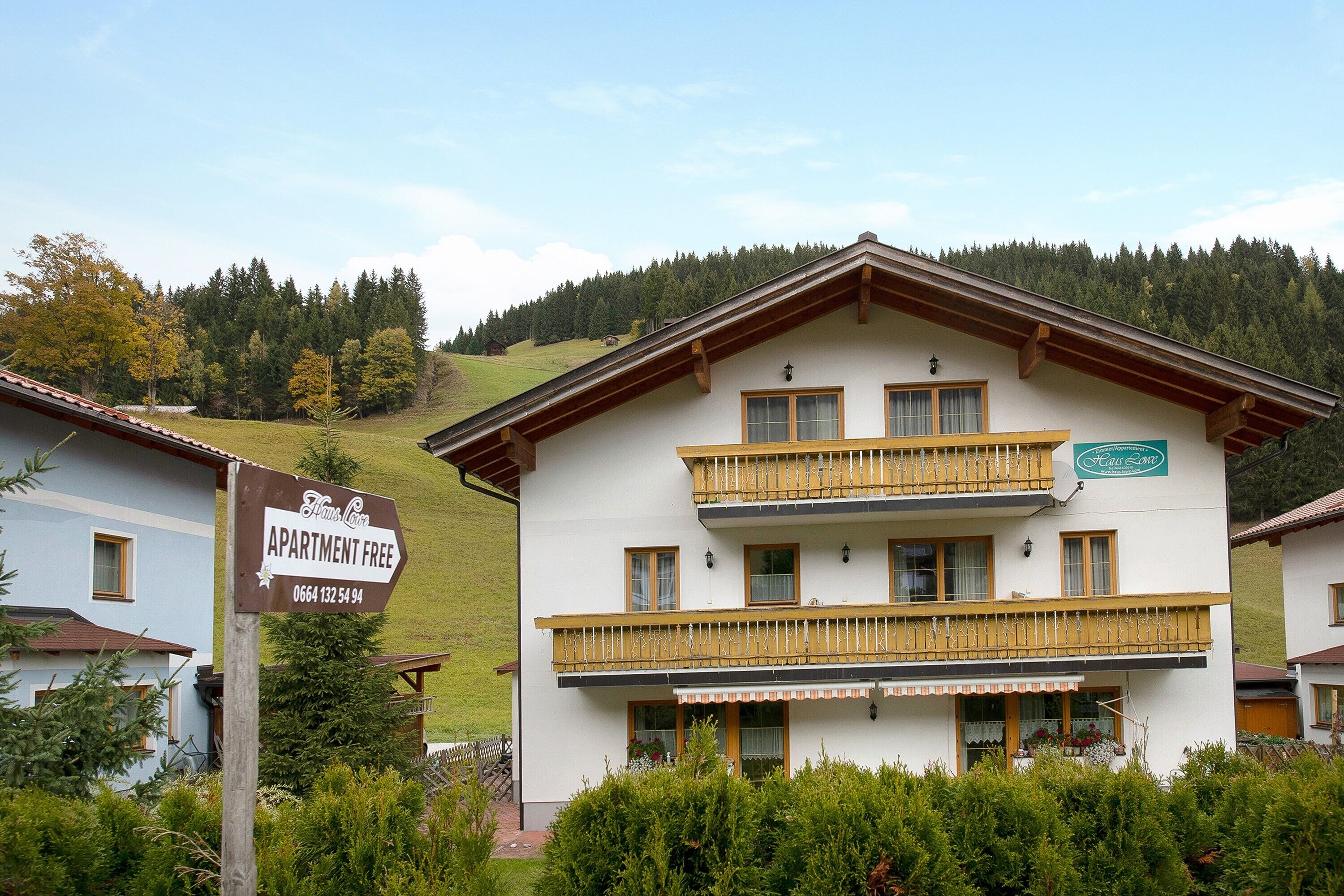 A multi-story building with balconies, a sign indicating 'Apartment Free,' and a view of a forested hillside.