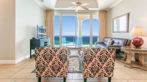 A living room with a view of the ocean, a ceiling fan, a television, and a sofa.