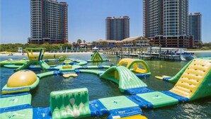 Un parque acuático con estructuras de juego inflables, un puerto deportivo con barcos y edificios altos al fondo.