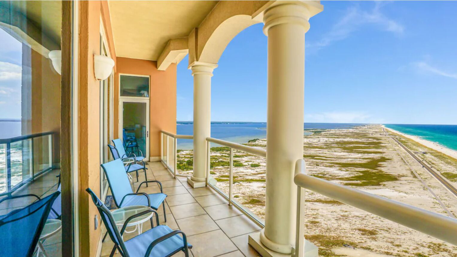 Een balkon met stoelen en tafels, met uitzicht op een strand en een heldere lucht.