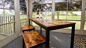 A room with a wooden table and bench, large windows with a view of trees, and a patterned rug.