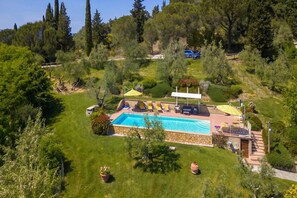 Une piscine dotée d’une plage en pierre, entourée d’une pelouse bien entretenue et d’arbres.