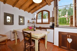 Una cocina rústica con una mesa de madera, sillas, una botella de vino y un ventanal con vistas a la vegetación.