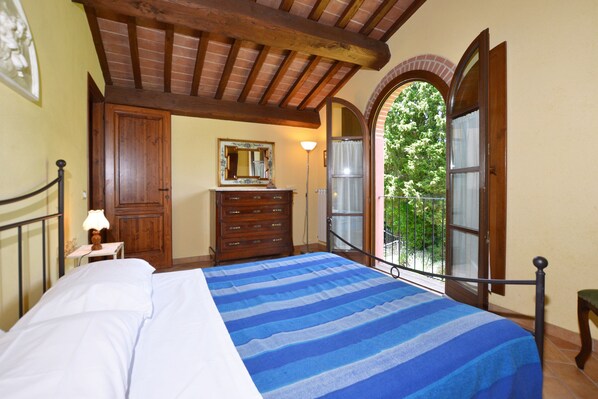 Une chambre avec un lit, une commode en bois et un balcon donnant sur un paysage verdoyant.