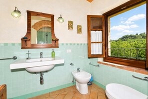 A bathroom with a sink, bidet, and toilet, a mirror, and a window with a view of greenery.