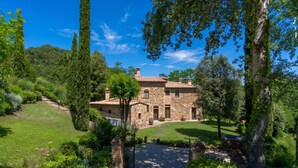 A stone house with a tiled roof, surrounded by lush greenery and a well-maintained lawn.