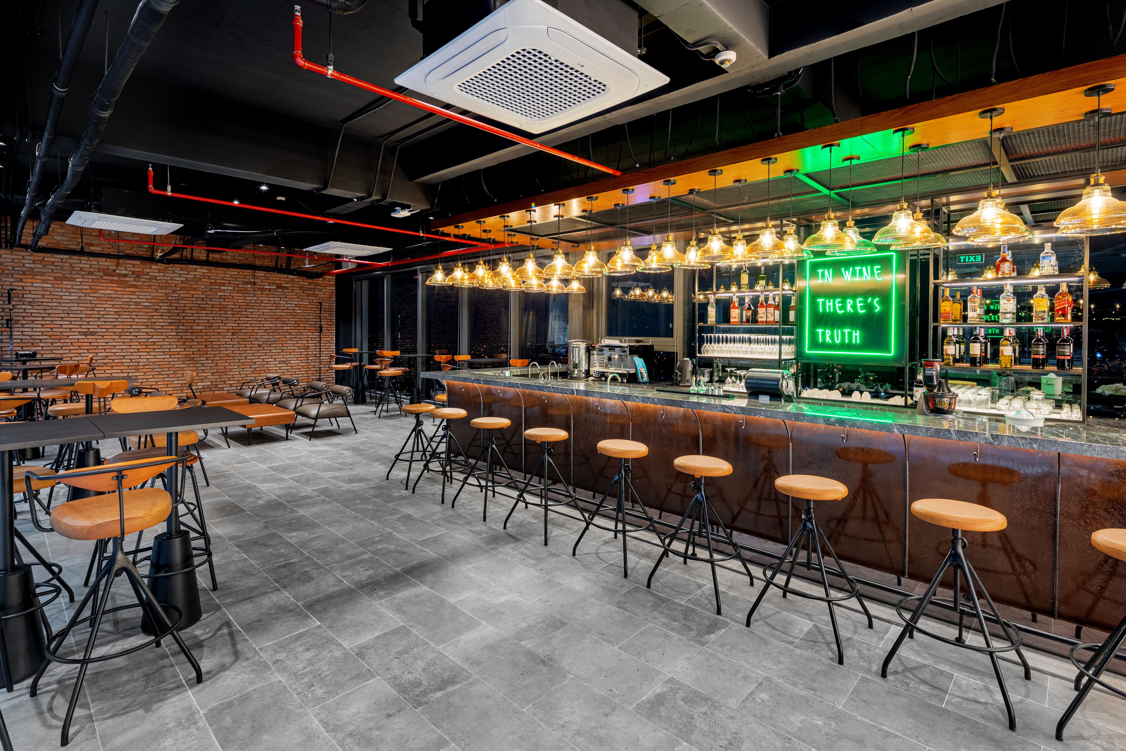 A bar area with stools, a neon sign, and a brick wall.