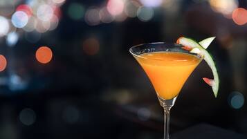 A cocktail in a martini glass with a garnish, set against a blurred cityscape background.
