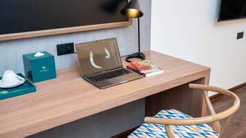 Un espacio de trabajo en un hotel con una computadora portátil, una caja de pañuelos, una bandeja con una taza, una lámpara y una silla.