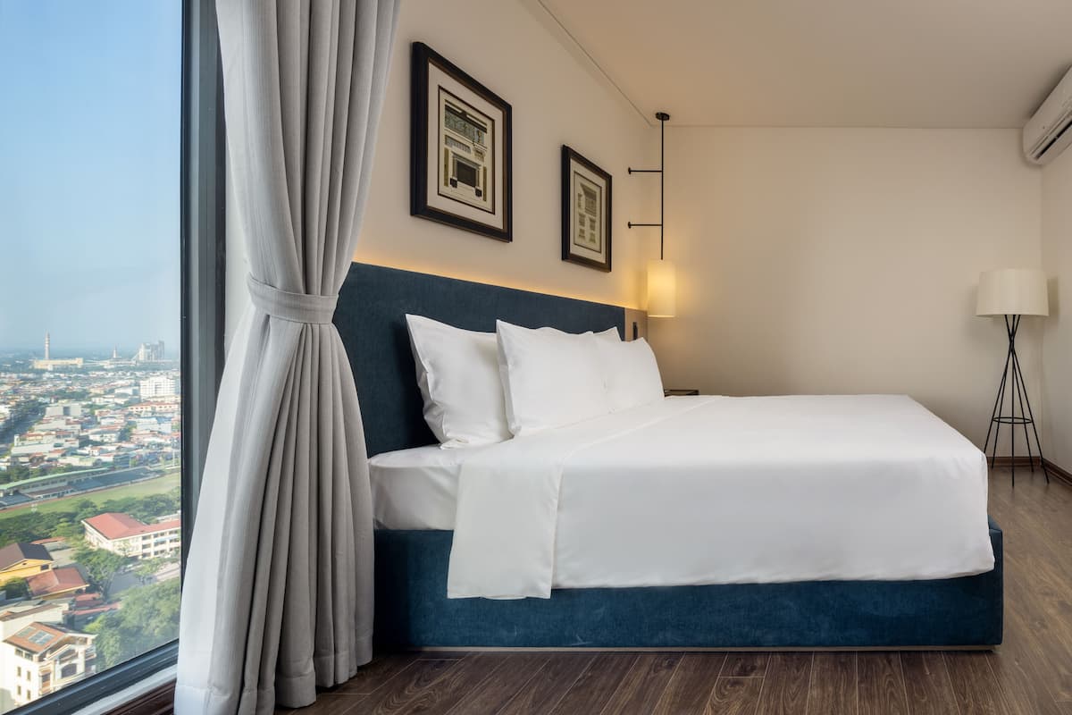 Habitación de hotel con una cama grande, vistas a la ciudad y una ventana con cortinas.