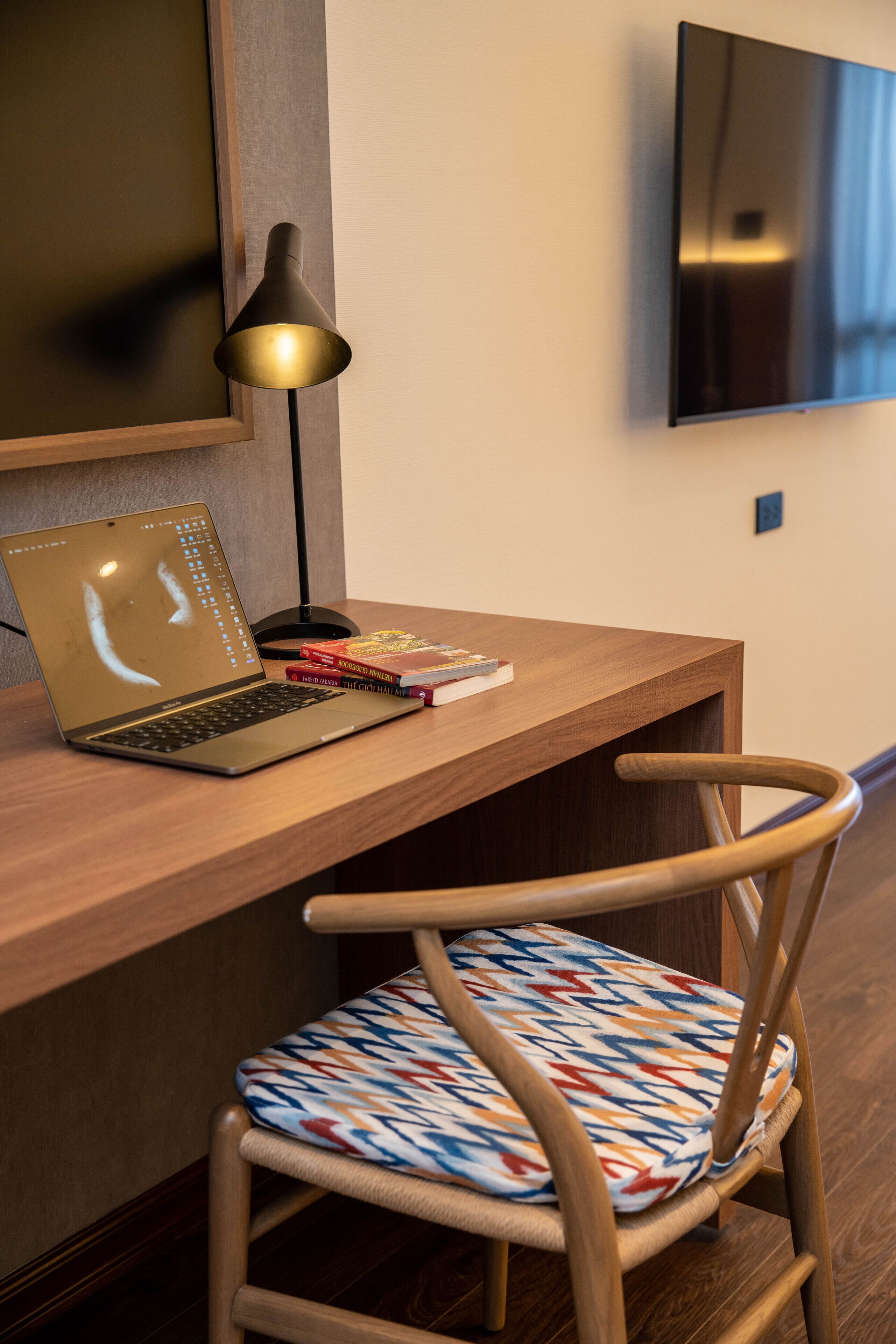 A wooden desk with a laptop, books, and a lamp.
