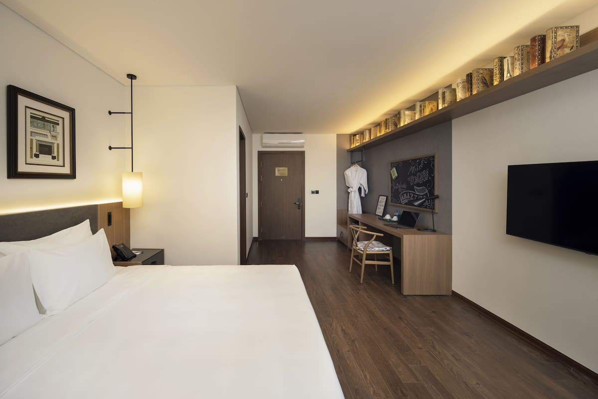 Habitación de hotel con una cama grande, un escritorio con silla, un televisor y una estantería decorada.
