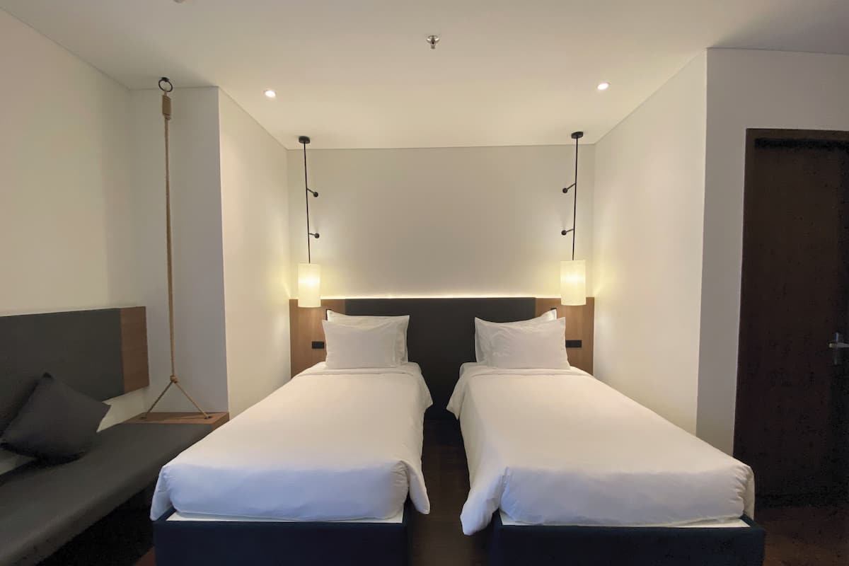 Una habitación de hotel con dos camas individuales, un sofá y una mesita de noche.