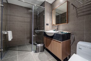 A modern bathroom with a glass shower enclosure, a sink with a black countertop, and a wooden vanity.