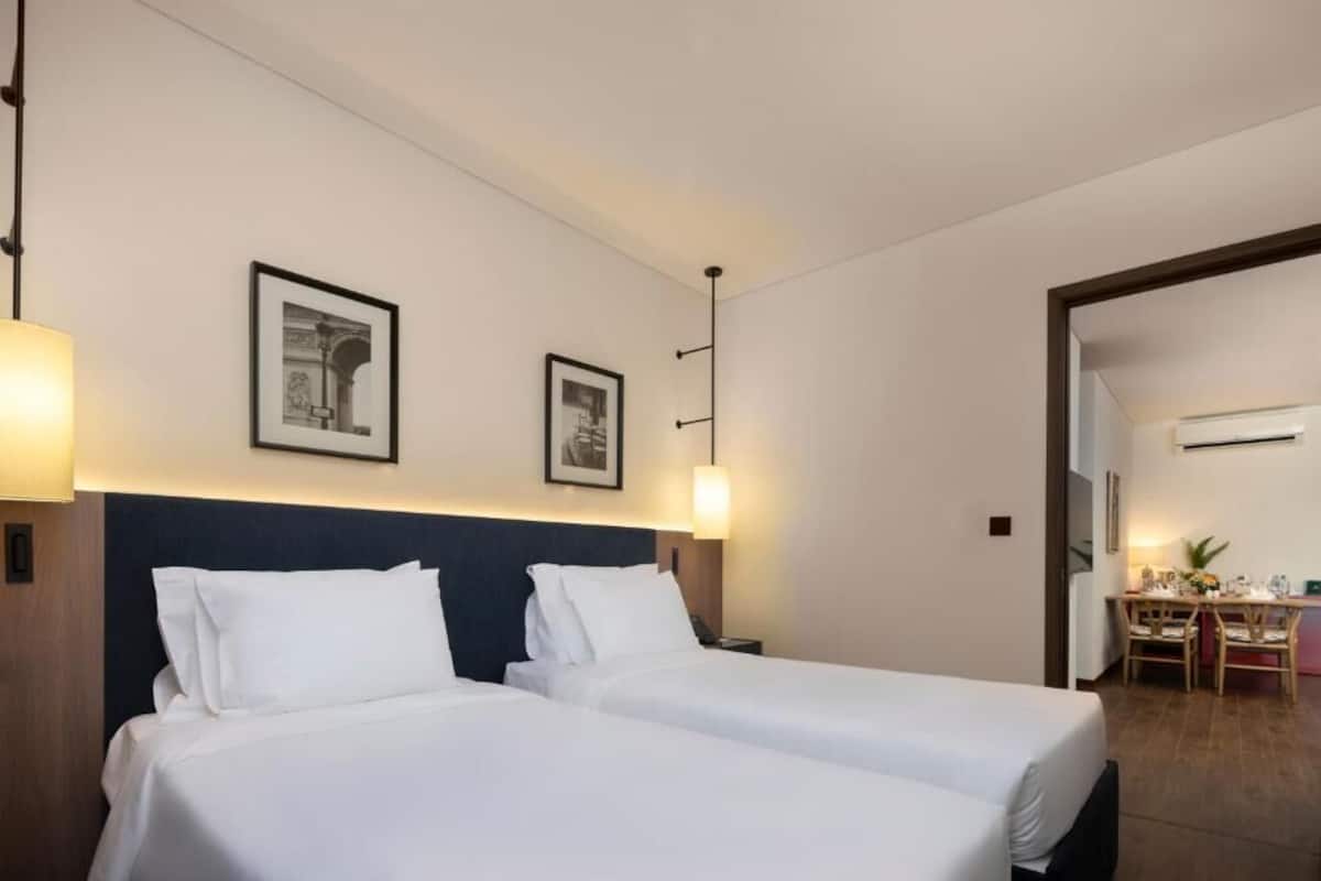 Una habitación de hotel con dos camas, un escritorio con sillas y cuadros en la pared.