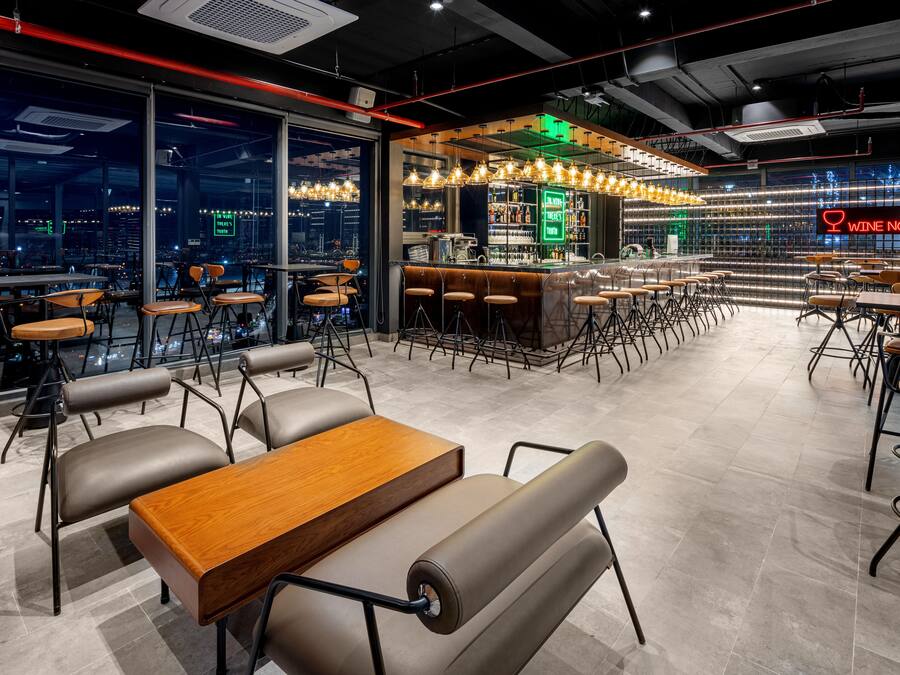 A modern bar area with a neon sign, seating arrangements, and a city view through large windows.