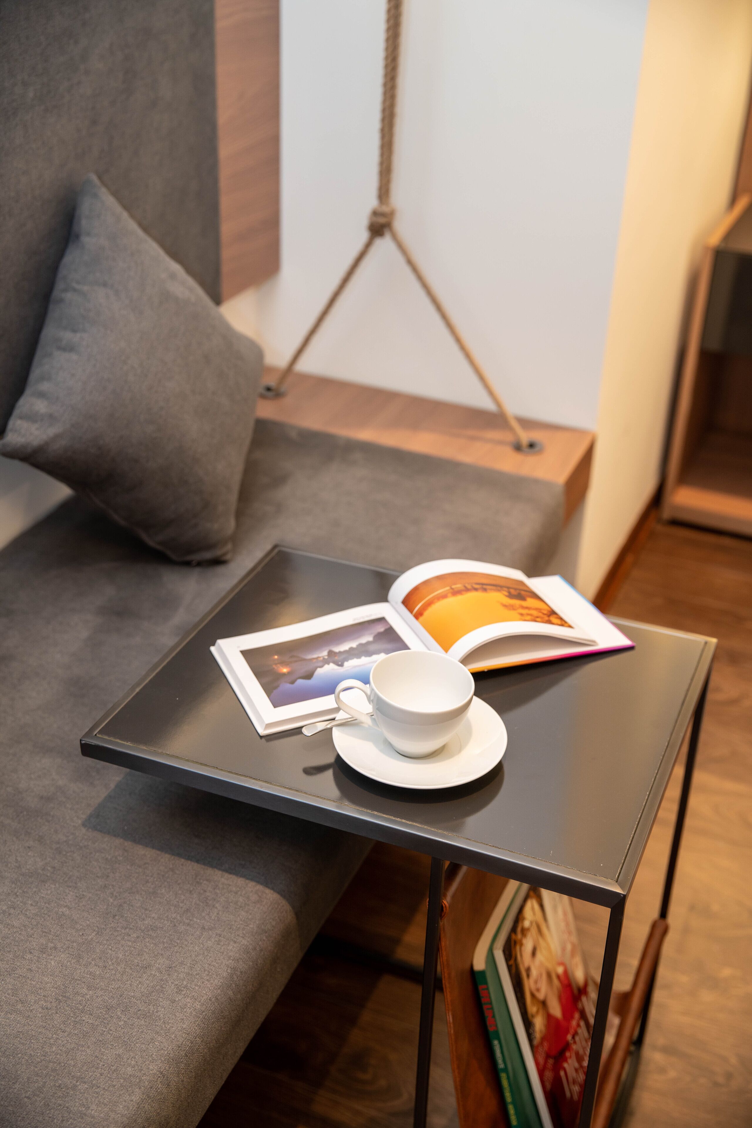 A small table with a cup, a book, and a magazine on a modern sofa.