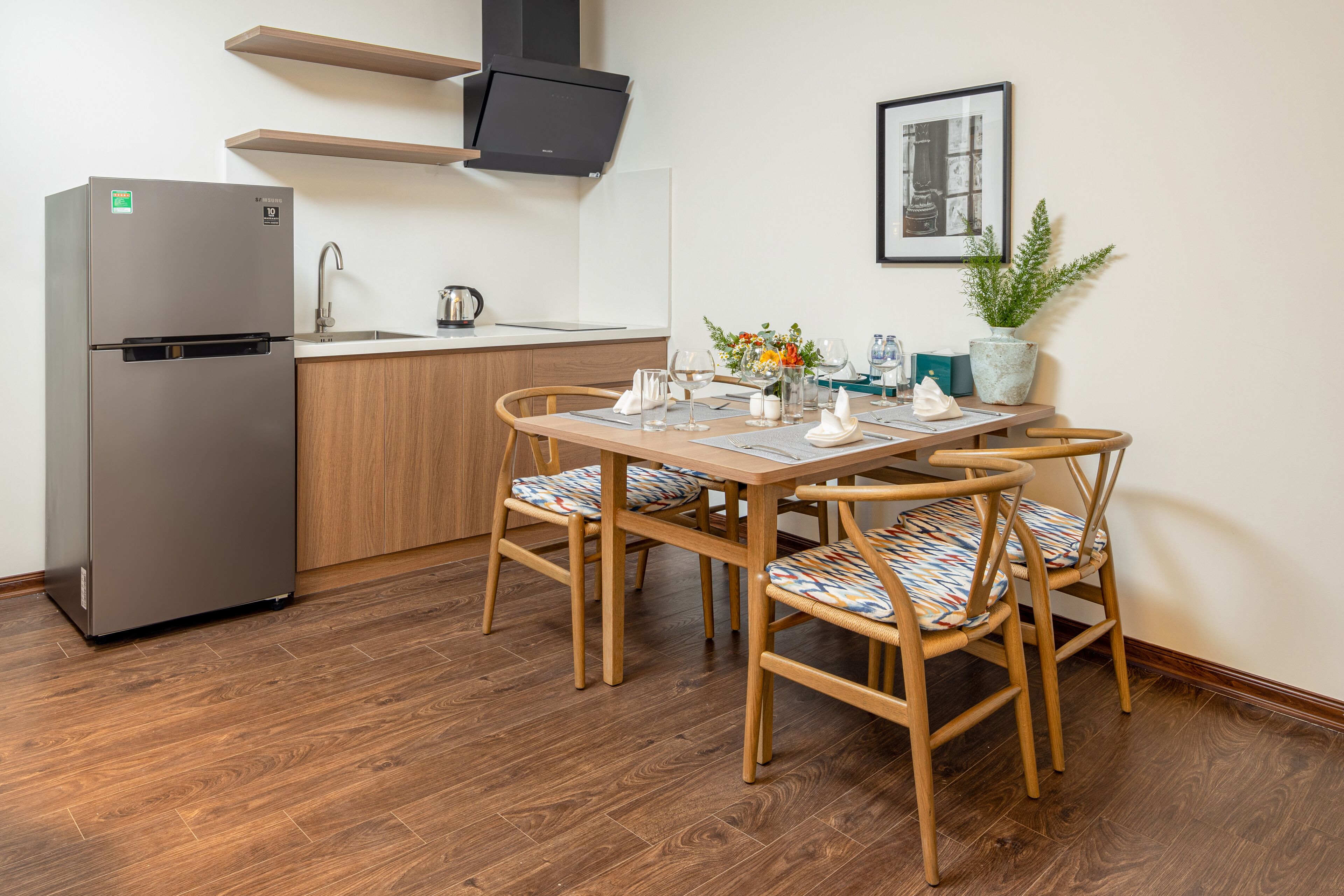 Une cuisine compacte dotée d’un réfrigérateur encastré, de meubles de rangement en bois et d’un coin repas avec une table et des chaises en bois.