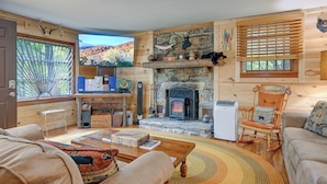 A cozy living room with a stone fireplace, wooden walls, a television, and a comfortable seating area.