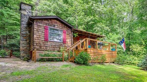 A rustic cabin with a stone chimney, wooden deck, and a flag.