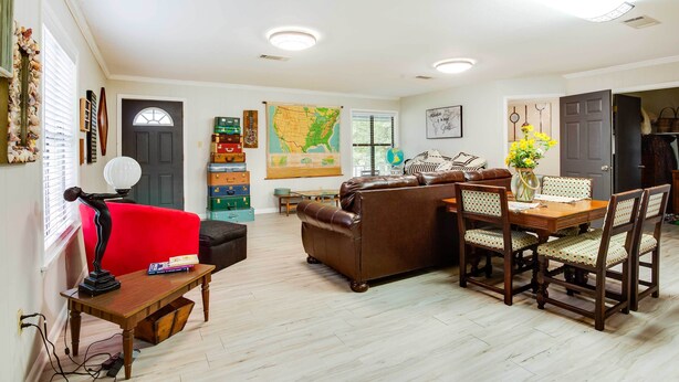 A spacious living room with a red sofa, a brown leather couch, and a wooden dining table with chairs. There is a map on the wall, a globe, and a lamp on a side table.
