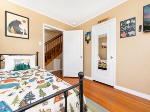 A bedroom with a bed, a wooden staircase, a door with a nameplate, and a wall with a picture.