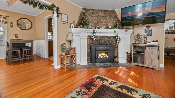 Una sala de estar con chimenea, piso de madera, televisor montado en la pared y adornos navideños.