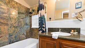 A bathroom with a marble wall, a bathtub, a wooden vanity with a sink, and a mirror. - Country Bear Inn - Game Room, Pool Table, Barbecue (Big Bear City)
