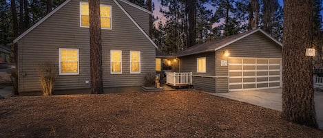 A two-story house with a garage, surrounded by tall trees and a well-maintained lawn.