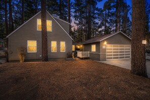 A two-story house with a garage, surrounded by tall trees and a well-maintained lawn.