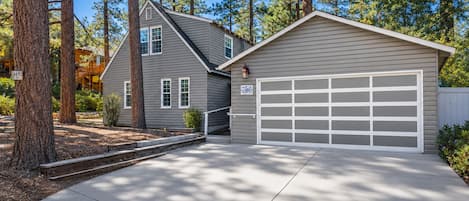 A two-story house with a garage, surrounded by tall pine trees.