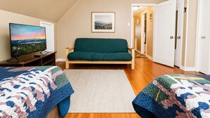 A room with a sofa, a television, and two beds with quilts. - Country Bear Inn - Game Room, Pool Table, Barbecue (Big Bear City)