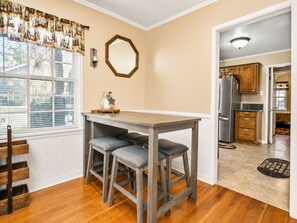 A kitchen with a wooden table and two stools, a refrigerator, and a window with blinds.