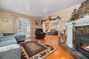 Una sala de estar con chimenea, un sofá, un sillón y un árbol de Navidad.