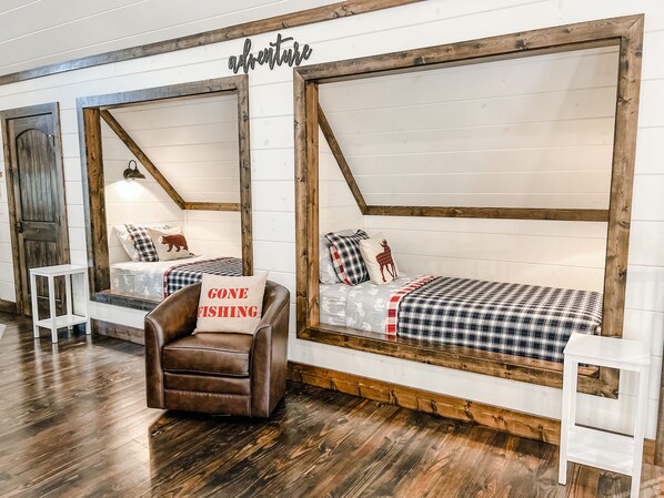 A cozy cabin-style room with two beds, a brown leather chair, and a 'Gone Fishing' pillow.