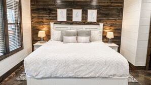Camera da letto con un letto grande, pareti in legno a pannelli, stampe botaniche incorniciate e una ventola a soffitto.
