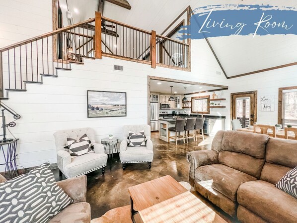 A spacious living room with a high ceiling, a staircase, and a kitchen area.