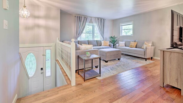 Un salón amplio con un sofá gris, una mesita y una escalera que conduce a una puerta con un vitral.