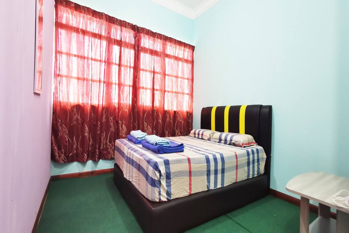 A room with a bed, a table, and a window with red curtains.